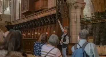 A volunteer speaking to a tour group and points at the Cathedral organ which has dark wooden and gold decorated pipes